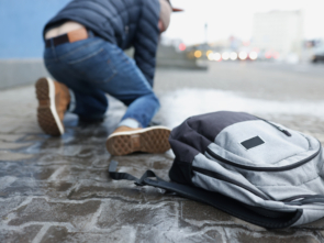 Backpack lying on slippery paving slabs near falling man, slip and fall accident